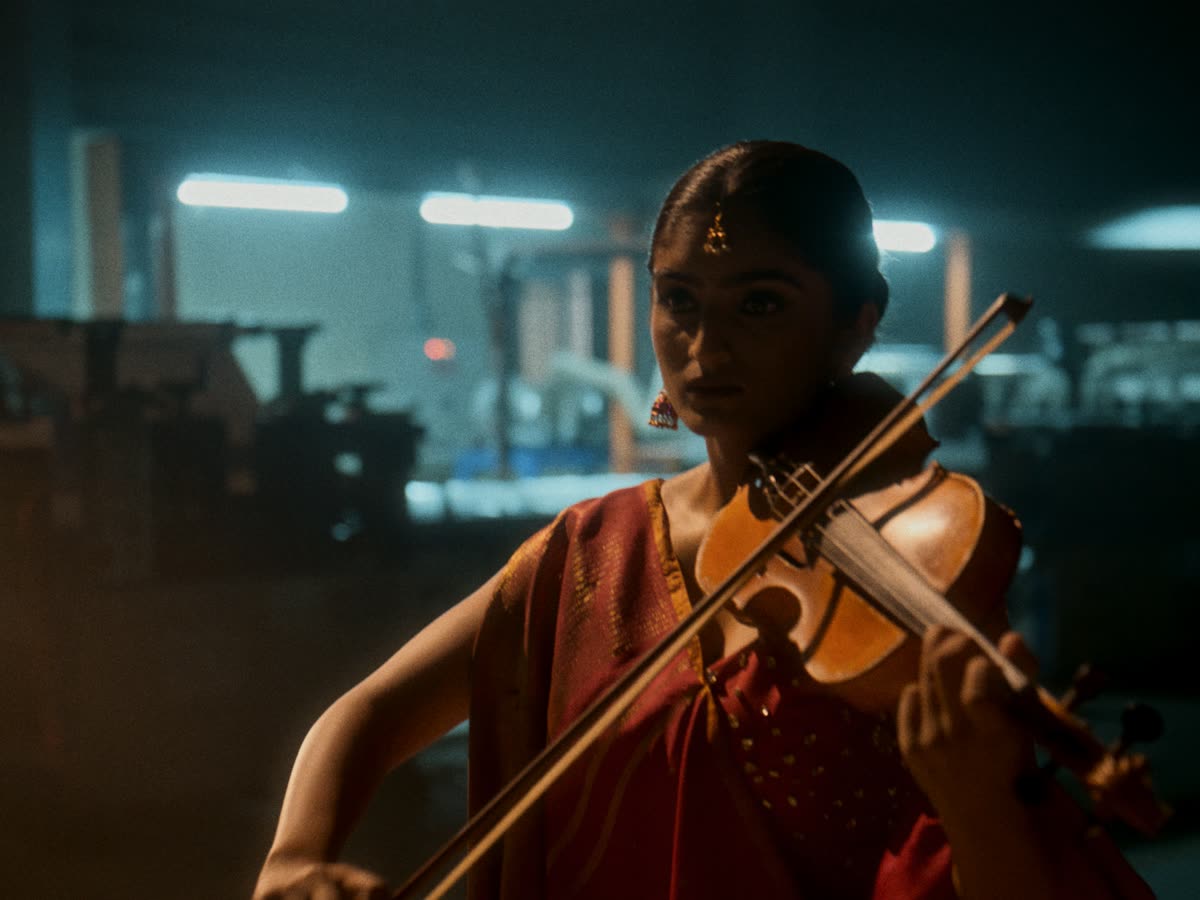 A violinist in red plays in a dark factory