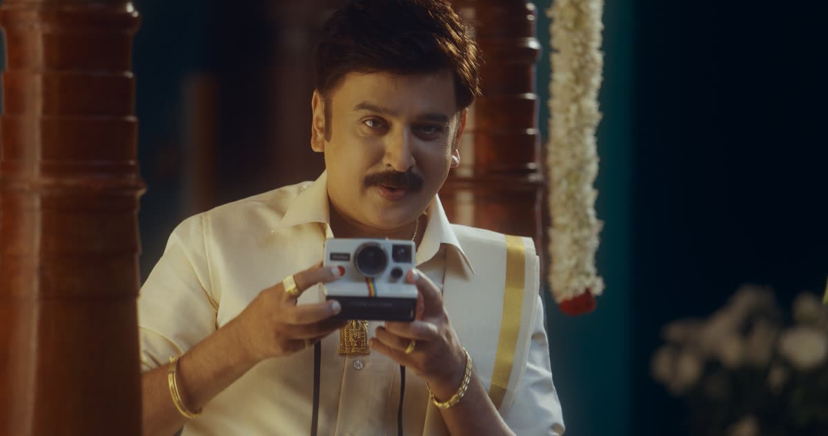 Ramesh Aravind in a white veshti holding an instant camera