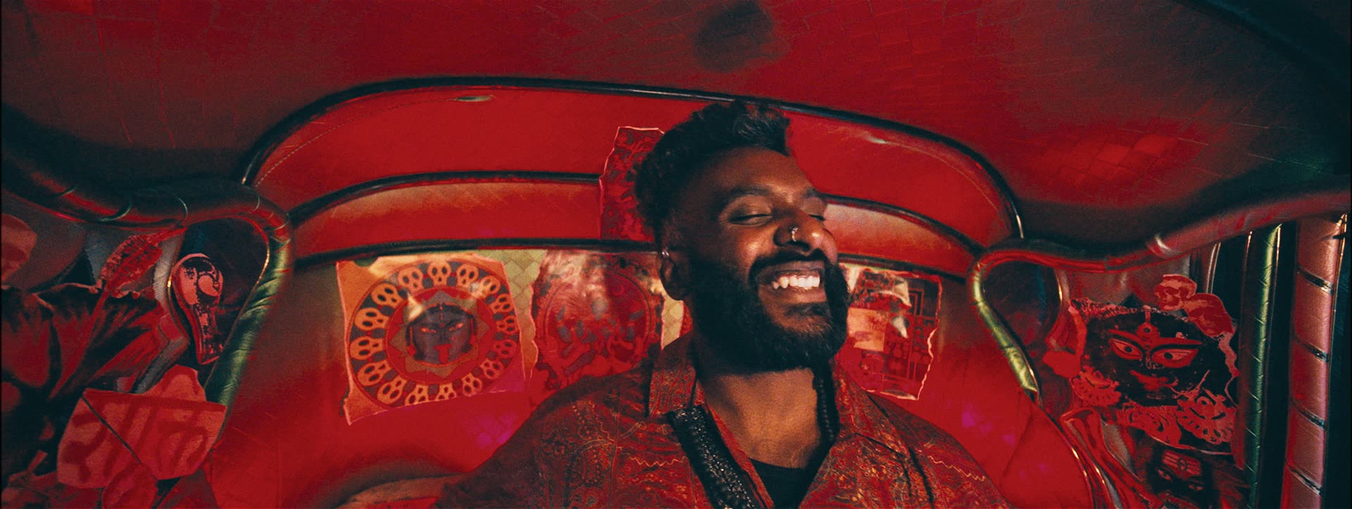 A rapper grins inside a red-lit auto-rickshaw